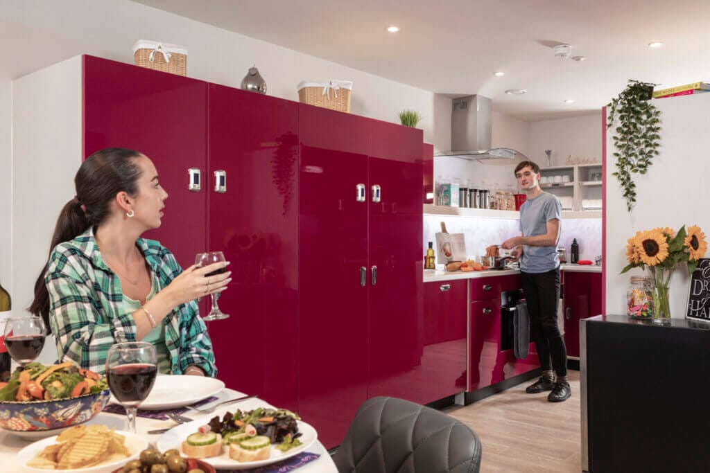 Study Inn Luxe Lounge in Leeds, a communal kitchen and living area where a student is cooking and the other is waiting for the food whilst drinking wine.