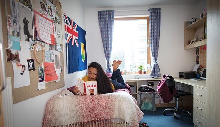 Student laying in bed reading a book at her University student accommodation.