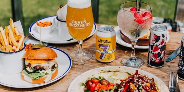 burgers, fries, beer, and cocktails set on a table outdoors