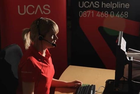 A UCAS support agent speaking on the phone during clearing, looking at a computer on her desk.