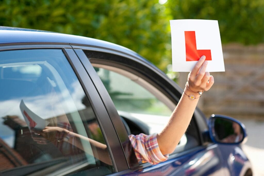 Driver holding a Learner sign out of the car.