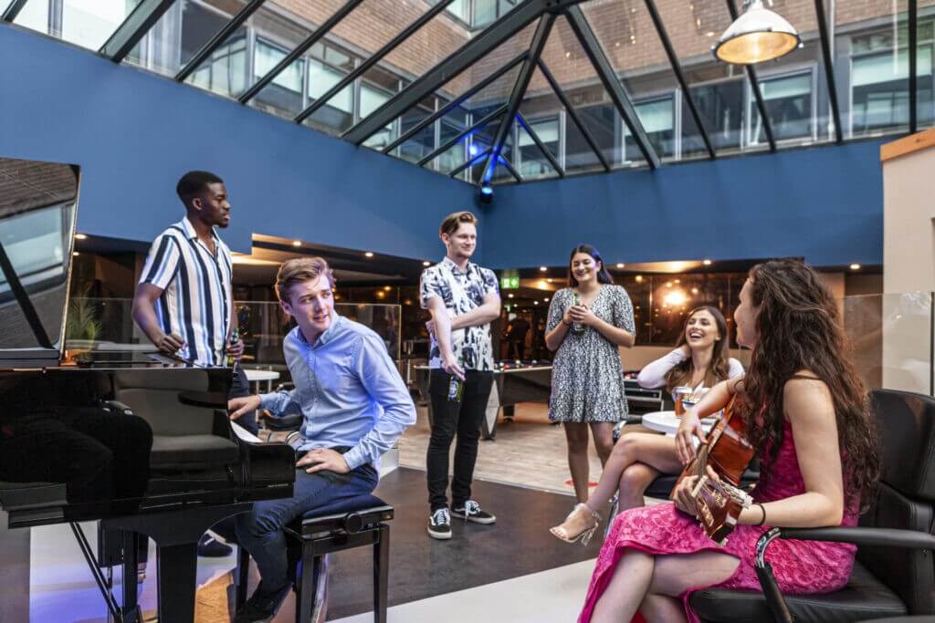 Resident students gathered around the piano having a good time, chatting, singing, and having a drink at one of Study Inn student accommodations.
