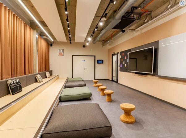 The Tannery's empty cinema room. Big screen and white board, as well as cork tables and sofas. Beige curtains hanging.
