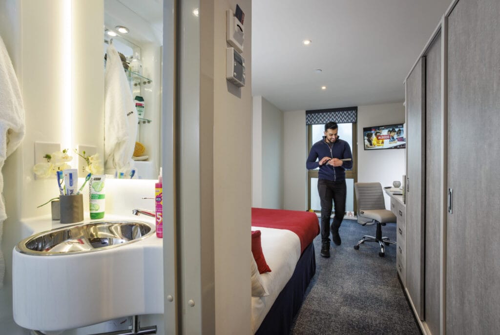 Study Inn Leeds, student accommodation in Leeds. Sapphire Plus apartment with student standing up reading a book in the room.