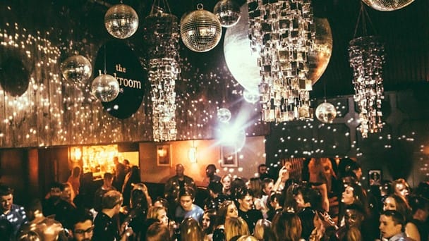 Leeds students dancing in a night club in Leeds. The room is dark, busy, and features many disco balls attached to the ceiling.