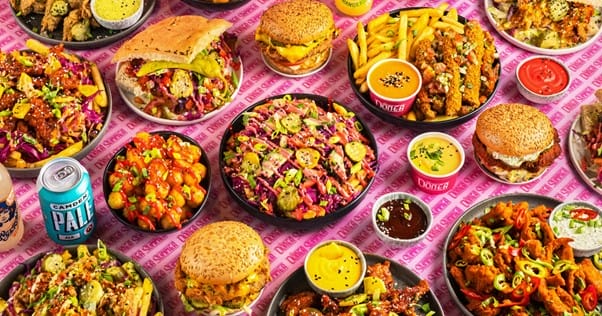 A pink table with many burgers, chicken, nachos, and dips.