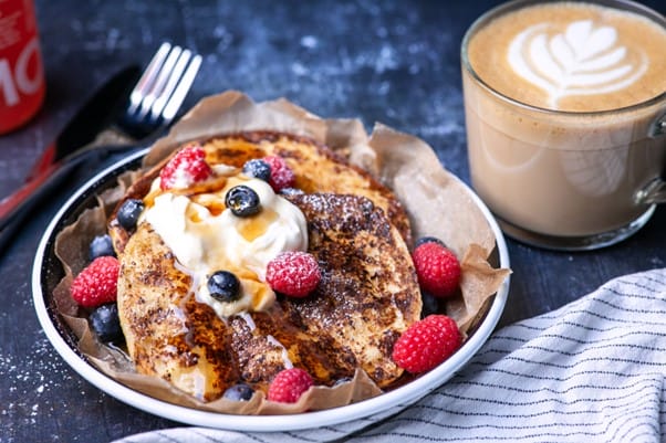Pancakes, yogurt, berries and honey on a table alongside a flat white drink.