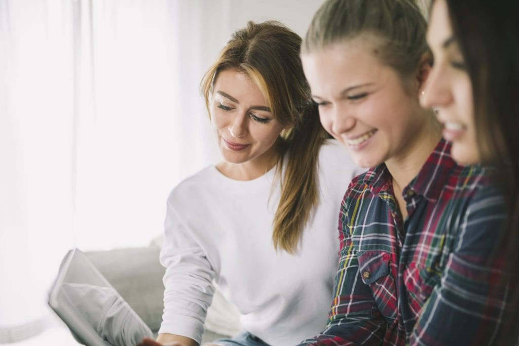 Group of young women smiling and looking at a laptop together for a student accommodation in Nottingham.