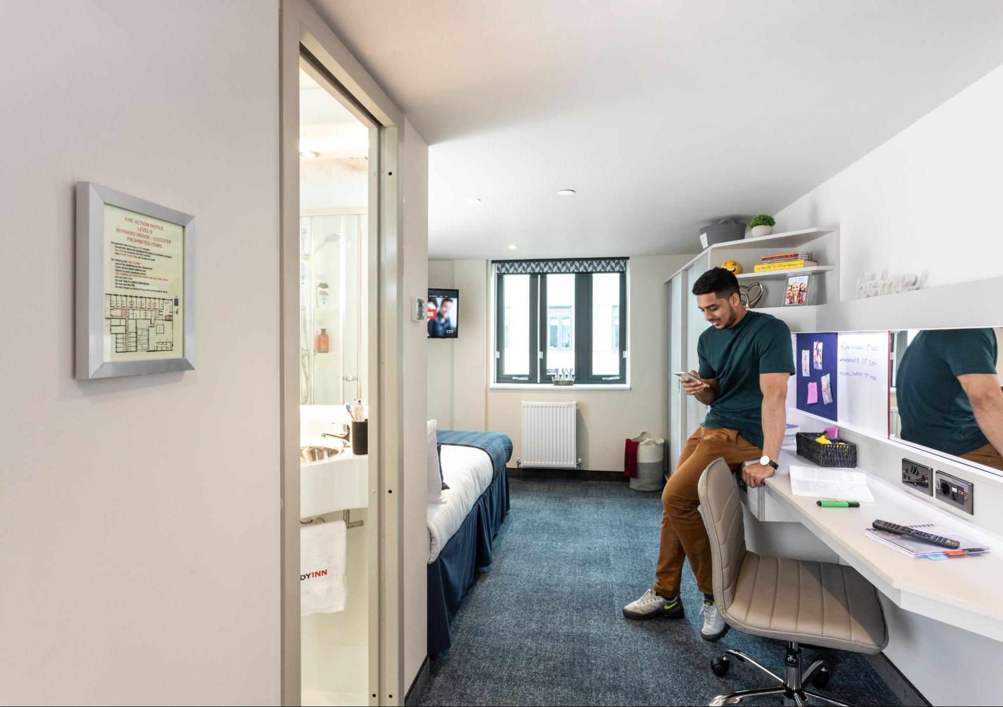 Student inside the Study Inn accommodation in Leicester, sitting on a desk chair while using a phone.