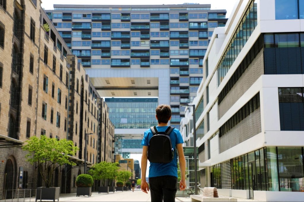A student with a backpack standing between modern city buildings